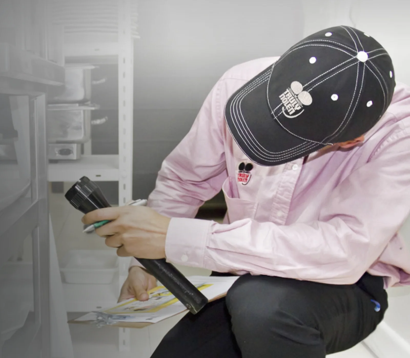 Técnico de Truly Nolen inspeccionando una instalación con linterna y registro de servicio
